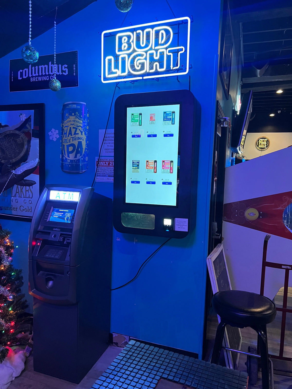 Wall mounted VTM vape vending machine installed in a bar beneath a Bud Light sign